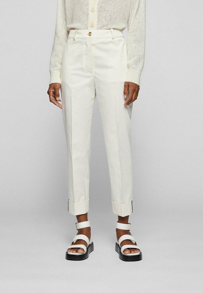 Białe, dopasowane spodnie o prostym kroju, z podwiniętymi mankietami i gładką fakturą, zestawione z masywnymi białymi sandałami.