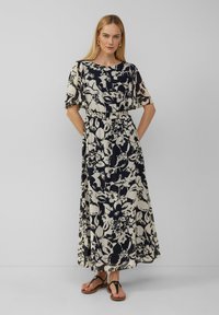 Maxi-Kleid in Creme mit einem marineblauen Blumenmuster. Kurze, lockere Ärmel, tailliert und lockere Passform. Getragen mit schwarzen Sandalen.