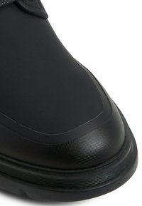 Botas negras impermeables con material superior liso, diseño de puntera redondeada, punta texturizada y suela de goma contrastante con surcos.