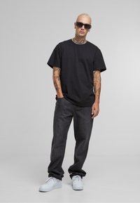 Černé bavlněné tričko s krátkými rukávy, spojené s tmavými džínami. Bílé tenisky dokončují outfit, doplněný slunečními brýlemi.