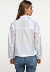 Witte satijnen jas met lange mouwen, een kraag en een rechte snit. Kenmerkt zich door een gladde textuur en een subtiele glans. Gecombineerd met denim.