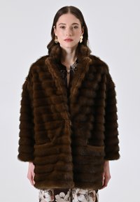 Cappotto di pelliccia marrone con una finitura morbida e testurizzata, caratterizzato da strisce orizzontali, un collo ampio e due tasche frontali.