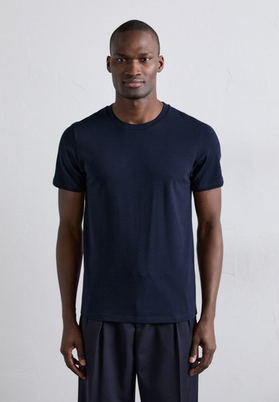 Marineblå kortærmet t-shirt lavet af blødt stof, med rund hals, minimalistisk design og en tætsiddende form. Kåret med mørke bukser.