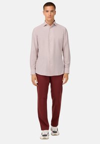 Camicia a maniche lunghe con bottoni di colore rosa chiaro, caratterizzata da un delicato motivo a righe verticali, abbinata a pantaloni di un borgogna scuro e scarpe da ginnastica bianche.