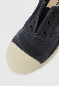 Scarpa da ginnastica in tela blu scuro con puntale in gomma. Presenta occhielli in metallo e suola bianca con texture. Nessun motivo o accento visibile.