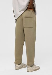 Beige katoenen joggingbroek met een relaxte fit, voorzien van een achterzak, ribgebreide tailleband en geborduurde enkels, gecombineerd met lichte sneakers.