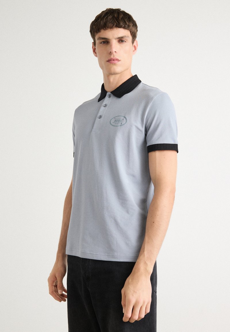 Lyseblå polo skjorte med svart krage, tre knapper og en liten logo på brystet. Korte ermer med svart kant.