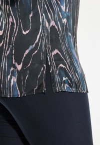 Blusa di satin con una base nera, caratterizzata da motivi astratti a onde rosa e blu. Spacco laterale e texture liscia, abbinata a pantaloni scuri.