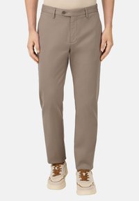 Pantalones beige hechos de una tela suave con corte recto, que cuentan con cierre de botón y bolsillos frontales, combinados con zapatillas deportivas blancas.
