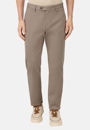 Beige Hosen aus glattem Stoff mit geradem Schnitt, ausgestattet mit einem Knopfverschluss und Taschen vorne, kombiniert mit weißen Sportschuhen.