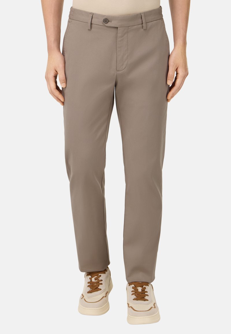 Pantalones beige hechos de una tela suave con corte recto, que cuentan con cierre de botón y bolsillos frontales, combinados con zapatillas deportivas blancas.
