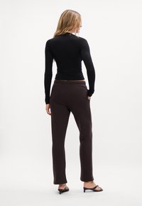 Melnas garas piedurknes blūze apvienota ar brūniem sporta biksēm. Blūzei ir pieguļoša forma; bikses ir taisnas kājas ar jostu, rādot gludu tekstūru.