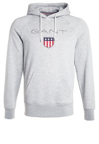 Sweat à capuche gris clair avec poche avant, cordons blancs, texte "GANT" et emblème de bouclier avec des bandes rouges et blanches et trois étoiles blanches.