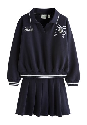 Pull polo bleu marine à manches longues avec poignets et ourlet à rayures blanches, associé à une jupe plissée assortie, avec des logos brodés blancs.