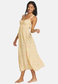 Maxime dress in kevyttä, keltasta kangasta, jossa on vaaleanpunaisia kukkakuoseja. Ominaisuuksiin kuuluu ohut olkaimet, nauhakiinnitys rinnan kohdalla ja virtaava siluetti.
