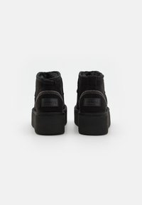 Zapatillas altas negras de ante texturizado, con suela de goma gruesa y costuras en contraste. Presenta un parche con un logotipo en la parte posterior.