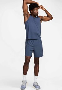 Nike'i sportlik komplekt, mis koosneb varrukateta tumesinisest toppist ja sobivatest lühikestest pükstest, valmistatud kergest kangast, millel on lõdvestunud lõige ja mugav disain.