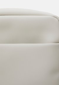 Schienale di sedia in pelle grigio chiaro o artificiale curvato, con superficie liscia e imbottita e bordi superiori arrotondati.