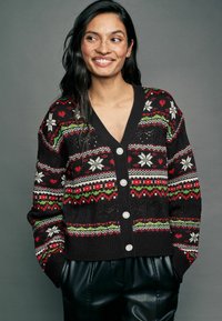 Sort strikket cardigan med festlige mønstre i rød, grøn og hvid, v-hals og seks dekorative knapper foran.
