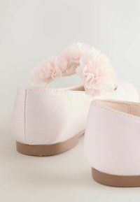 Šviesiai rožiniai baleto bateliai su minkštu satino paviršiumi, papuošti gėlių akcentu gale ir paprastu, plokščiu padu.