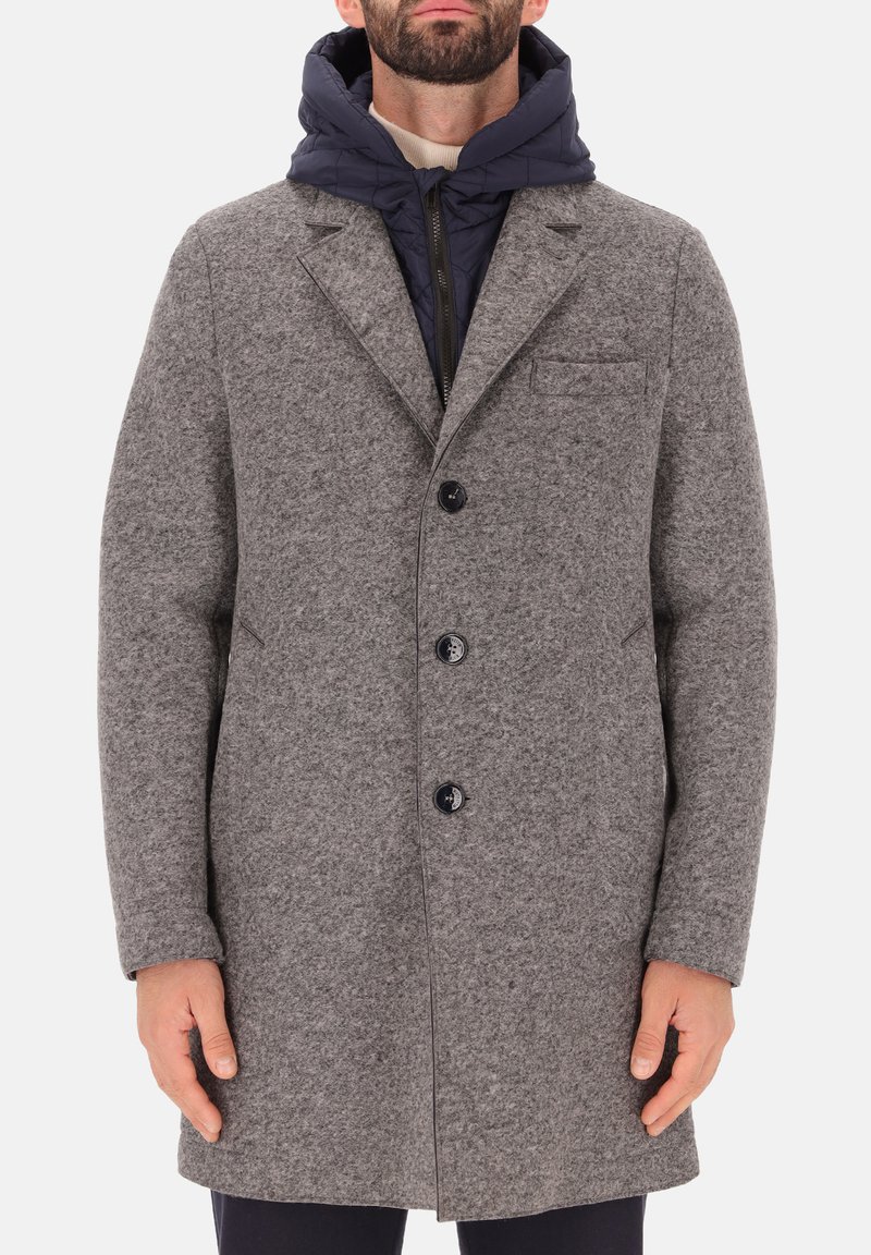 Cappotto grigio in misto lana con colletto a scollo, tre bottoni neri e una tasca sul petto, indossato sopra un hoodie blu imbottito.
