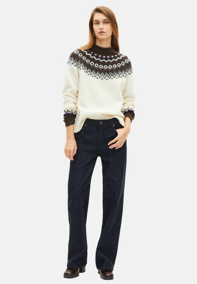 Sweater de malha com um corpo creme, yoke de padrão escuro e punhos canelados; combinado com jeans de perna larga azul escuro e calçado castanho.