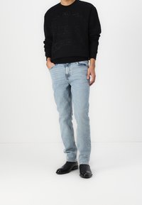 Black sweatshirt with textured logo, light blue jeans, and black ankle boots. Casual outfit featuring relaxed fit and subtle detailing.