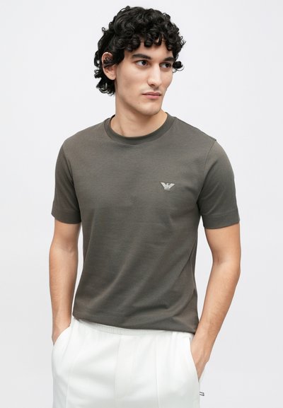 Krátke rukávy tričko olivovo zelenej farby vyrobené z ľahkej látky, s okrúhlym výstrihom a malým logom na ľavej strane hrudníka.