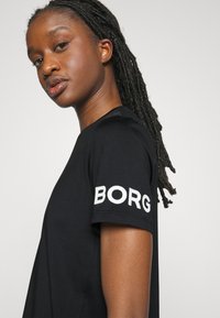 Črna bombažna majica s krožnim izrezom, ki ima na levem rokavu bele vezenine z besedilom "BORG". Gladka tekstura in zasnova s pravilno prileganje.