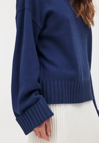 Navy blue knitted sweater featuring a ribbed hem and cuffs, with a loose fit. Close-up of the fabric texture highlights its softness.