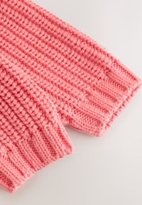 Gros plan d'un tissu tricoté rose épais affichant des mailles côtelées et texturées épaisses sur un matériau doux.