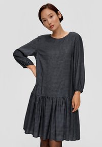 Dunkelblaues Kleid mit langen Ärmeln; verfügt über ein Hahnentritt-Muster, einen runden Ausschnitt und einen ausgestellten Rüschensaum für zusätzlichen Volumen.