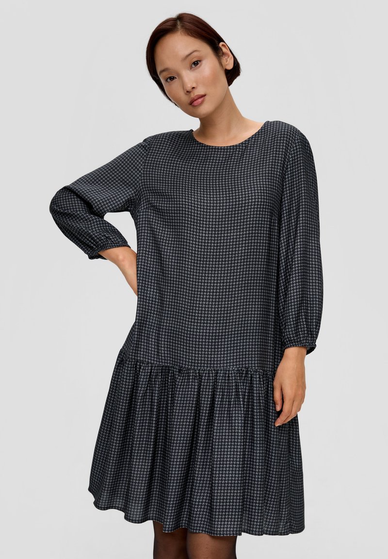 Donkerblauwe jurk met lange mouwen; beschikt over een houndstooth-patroon, ronde halslijn en een uitlopende rimpelige zoom voor extra volume.