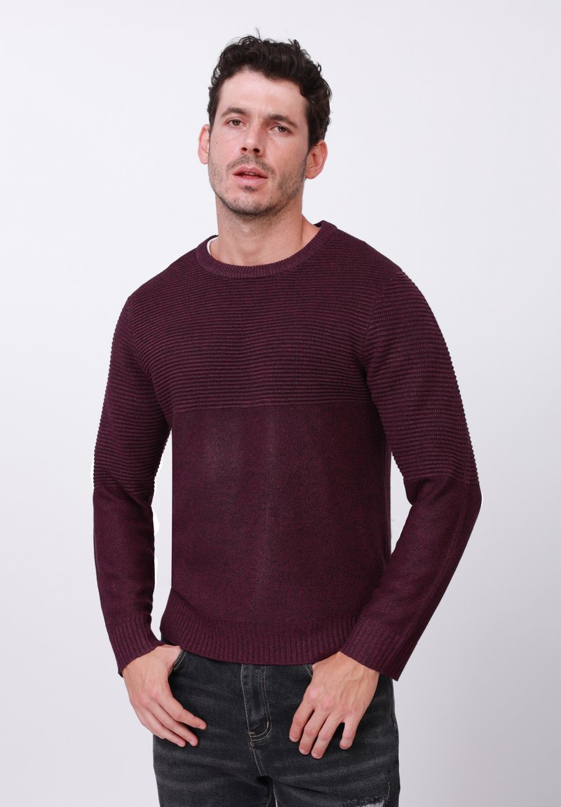 Pull en tricot bordeaux avec texture côtelée, col rond et manches longues. Le matériau semble doux, avec une section lisse contrastante à la taille.