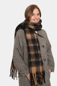 Rutigt halsduk i svart och brunt, gjord av mjukt tyg med fransiga ändar. Den är virad runt en texturerad kappa med stora knappar.