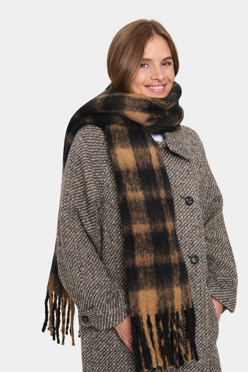 Rutigt halsduk i svart och brunt, gjord av mjukt tyg med fransiga ändar. Den är virad runt en texturerad kappa med stora knappar.