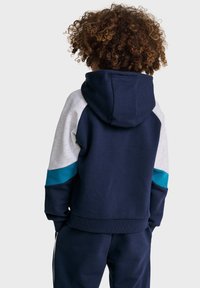 Felpa con cappuccio navy, maniche a blocchi di colore grigio e teal. Materiale in cotone, polsini e orlo a costine. Dotata di tasca a marsupio.