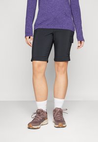 Mustad mustad lühikesed püksid, mis on slim fit stiilis ja külgmise cargo taskuga, koos lillat värvi pikkade varrukatega toppi ja pruunide matkajalatsitega. Valged ankur sokid on nähtavad.