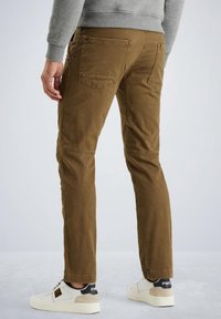 Pantalones de algodón marrón con corte recto, bolsillos traseros visibles y una sutil textura, combinados con zapatillas blancas con acentos negros.