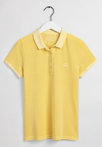 Chemise polo jaune sur un cintre avec des manches courtes, dotée d'un col classique, d'une patte de boutonnage à trois boutons et d'un petit logo sur la poitrine.