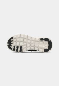 Semelle de chaussure de sport noire avec motif de grip texturé, comprenant une semelle intermédiaire blanche et un design segmenté distinct pour la flexibilité et l'adhérence.