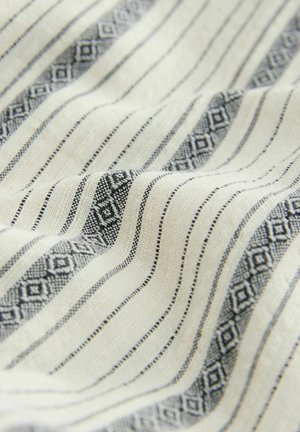 Textil mit cremefarbener Basis, schwarzen Linienstreifen und geometrischen Mustern. Weiche Textur, gewebtes Design mit variierenden Mustern und Farben.