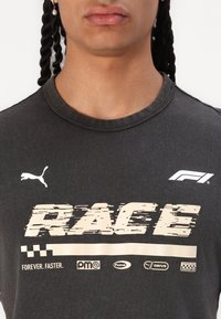 Anglies pilkos spalvos marškinėliai su nusidėvėjusiu kreminės spalvos užrašu "RACE", logotipais ir šachmatų printu. Trumpomis rankovėmis ir apvalia iškirpte.