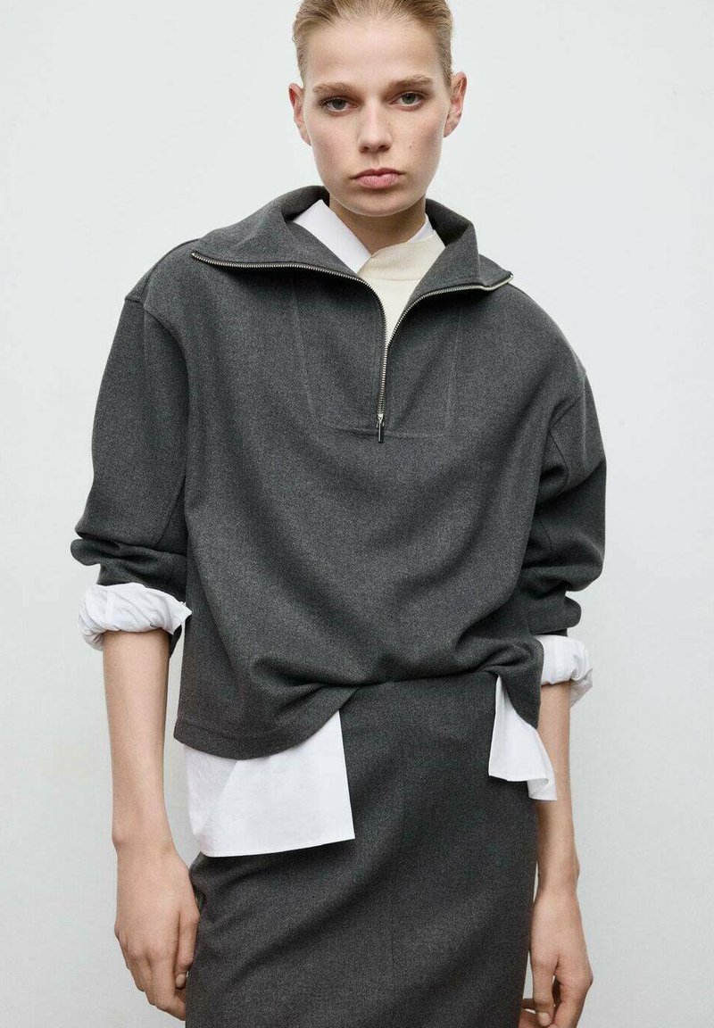 Gray zip-up sweatshirt with a wide collar, made of soft fabric. Layered over a white shirt, features long sleeves with rolled cuffs.