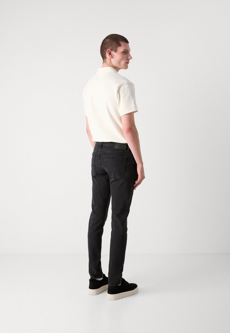 Czarne jeansy męskie o slim fit z delikatnym wypłowieniem, w połączeniu z beżową koszulką polo. Model nosi czarne buty z kremową podeszwą.