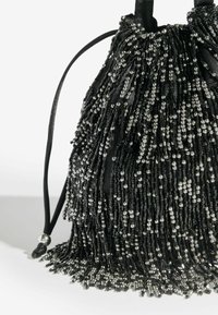 Mustikkahelmin koristeltu vetoketjullinen laukku, jossa on hopeiset yksityiskohdat. Laukussa on erilaisista helmitekstuureista ja materiaaleista valmistettu fringetyyli.