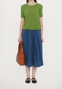 Maglione verde a maniche corte, gonna di denim larga, borsa a tracolla intrecciata marrone e ballerine nere. Presenta una texture liscia e un design casual.