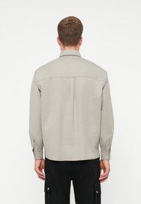 Ανοιχτό γκρι πουκάμισο με γιακά, πλισέ στην πλάτη και μακριά μανίκια, φο�ρεμένο πάνω από μαύρο cargo παντελόνι. Λείο υφασματικό υφασμά.