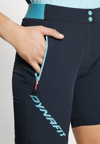 Shorts sportivi neri con una fascia in vita azzurro chiaro e dettagli. Le caratteristiche includono una tasca con zip con un tirante arancione e un logo sul lato.