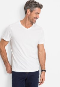 T-shirt bianco a maniche corte con scollo a V realizzato in cotone, caratterizzato da una texture liscia e una vestibilità classica, abbinato a jeans in denim scuro.
